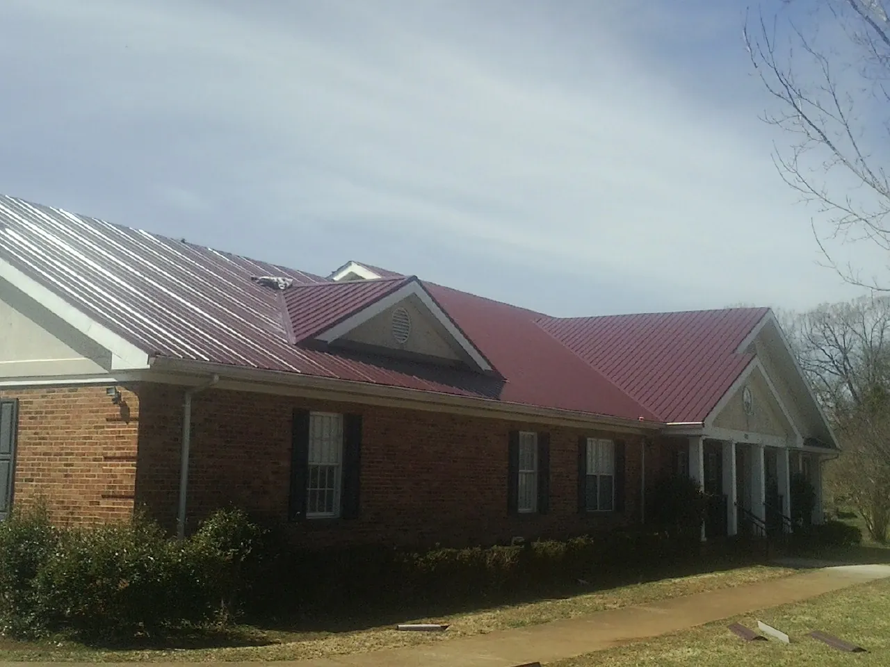 Red metal roof with gabled entries on a long brick building, from a Hail Damage Roof Repair job in Brooklyn