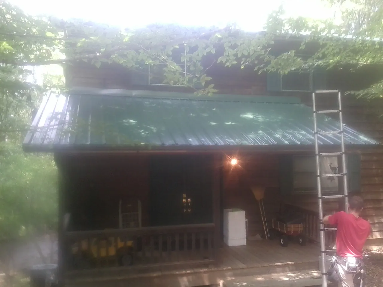 Worker on a ladder at the green porch roof of a wooded cabin in Brooklyn
